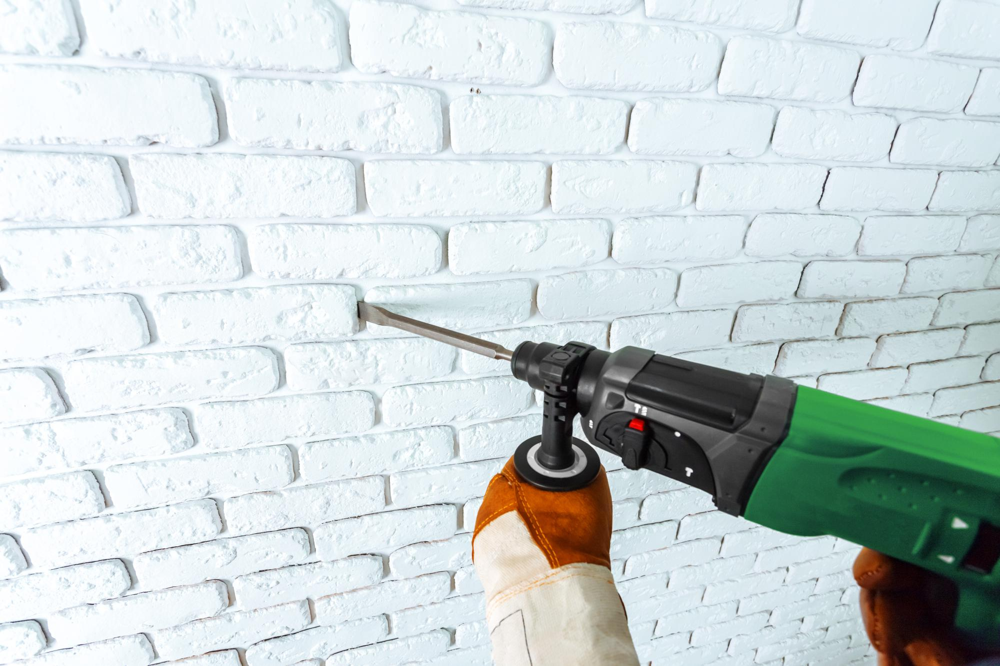 Ouvrier lj rénovant un mur en brique à la perceuse à joints dans une maison à gimont