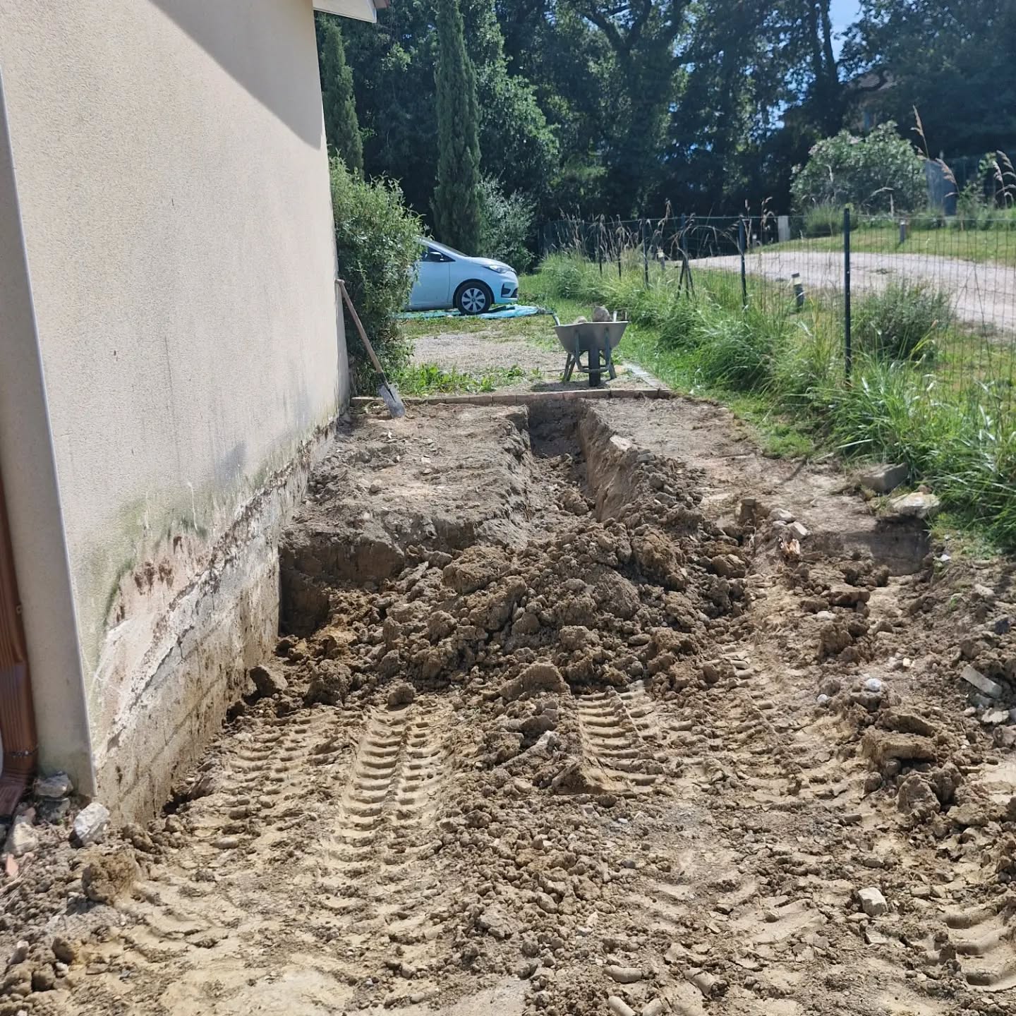 terrassement de jardin par lj à gimont, tranchée le long d’une maison avec outils et végétation en été